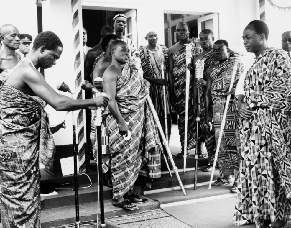 Kente and the Politics of Being Read 7 Kwame Nkrumah in patterned cloth standing among chiefs in kente outside a building, black-and-white photograph.