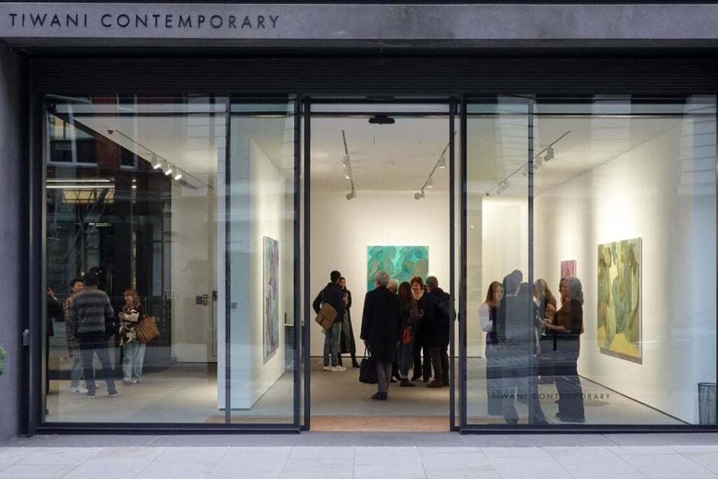 What the Closure of Tiwani Contemporary Reveals About the African Art Market 5 Evening view of the Tiwani Contemporary gallery storefront in London, visitors gathered inside among paintings during an exhibition opening