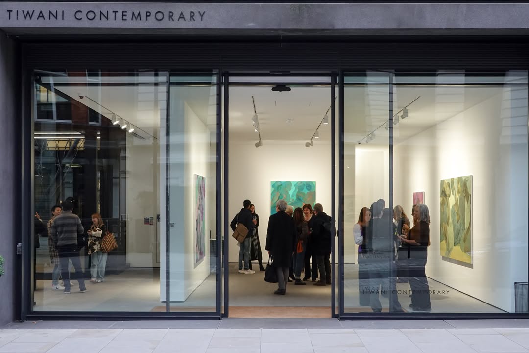 Evening view of the Tiwani Contemporary gallery storefront in London, visitors gathered inside among paintings during an exhibition opening