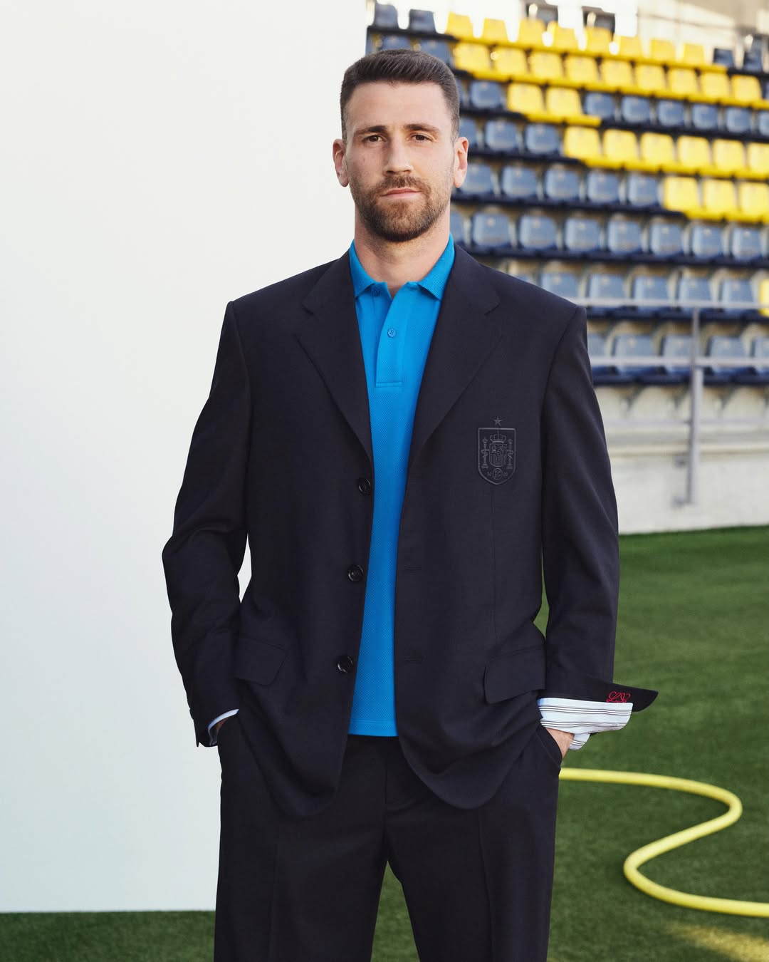 Loewe x Spain travel wardrobe: navy blazer over a blue polo, worn pitchside ahead of the 2026 World Cup.