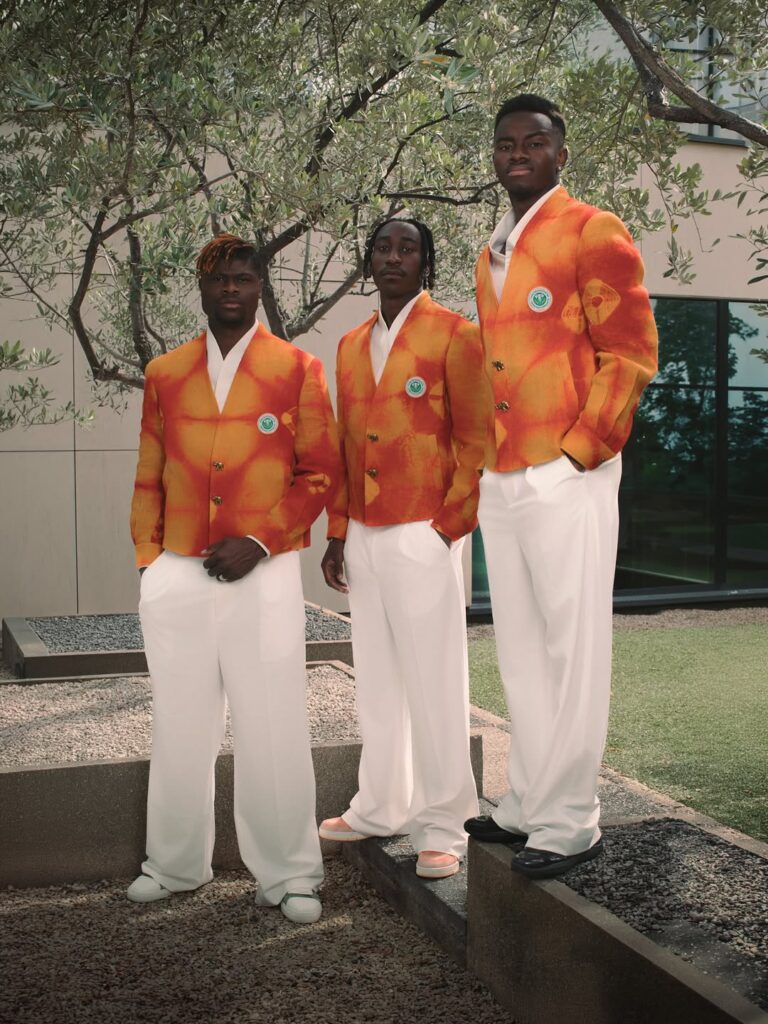 If This. Then That: World Cup Edition — Dressing the Team — Loewe → Ibrahim Fernandez 5 Three men standing in Ibrahim Fernandez's saffron-orange ceremonial jackets and white trousers, Cote d'Ivoire's off-pitch World Cup look.