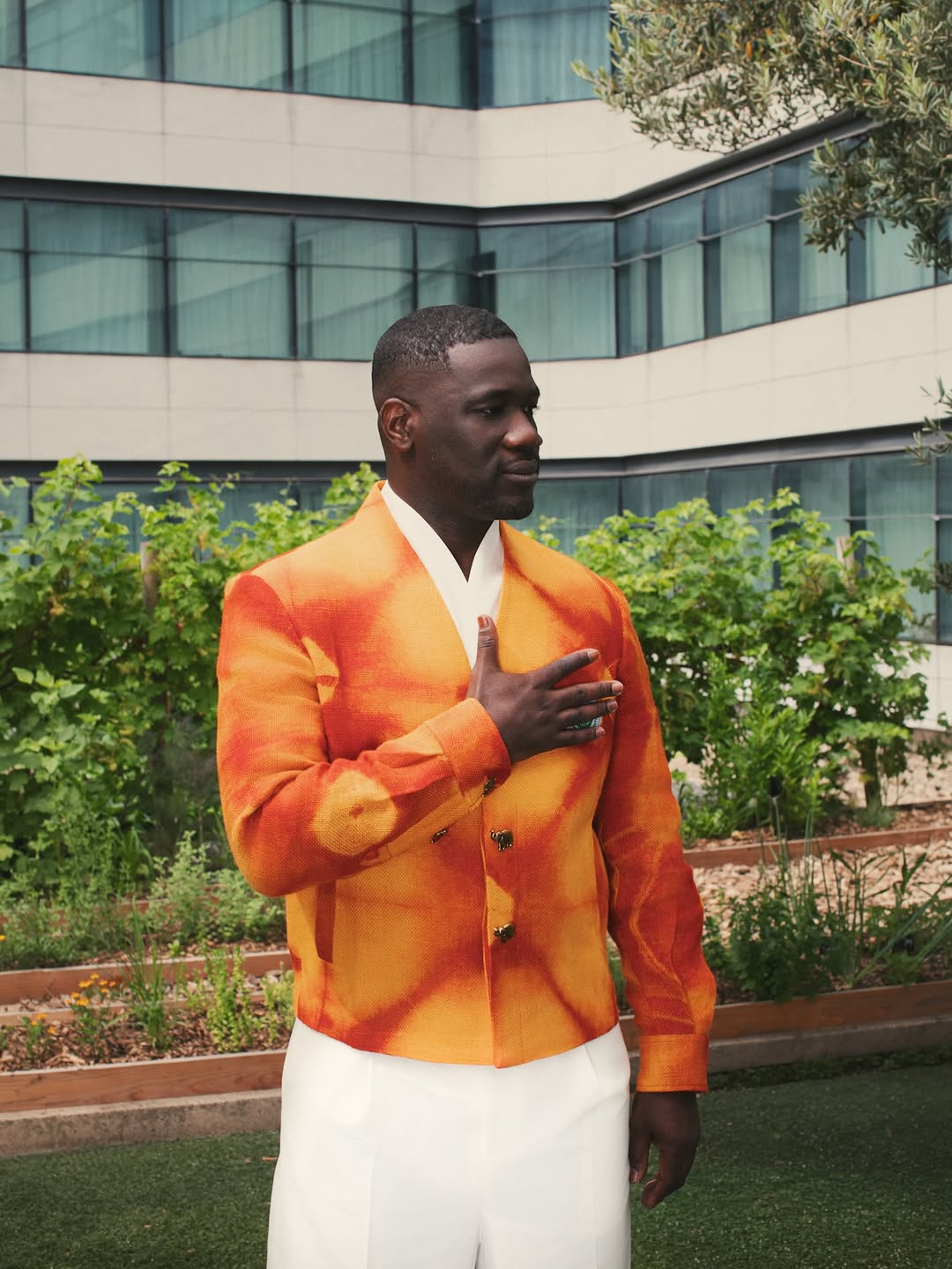 A man in Ibrahim Fernandez's structured saffron-orange ceremonial jacket and white trousers, Cote d'Ivoire's off-pitch World Cup look by the Ivorian designer.