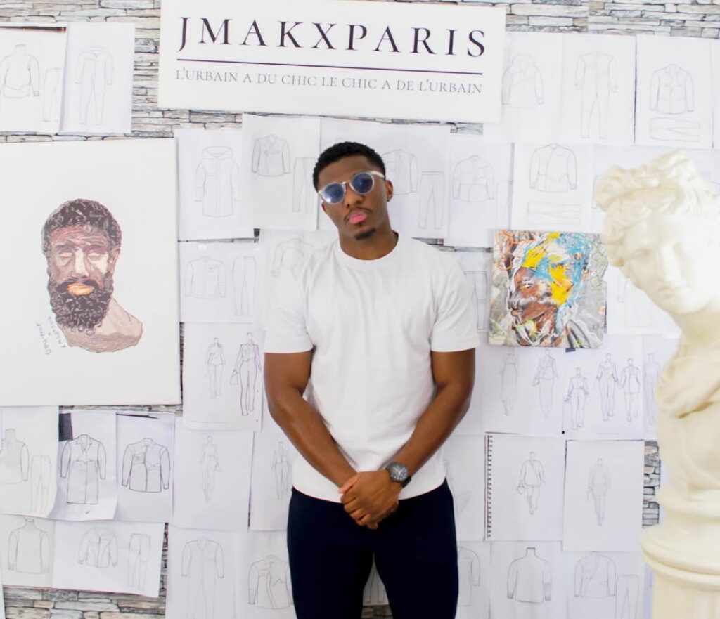 Alvin Junior Mak, founder of the Paris fashion label JMAKxPARIS, standing in his studio in front of a wall of garment sketches