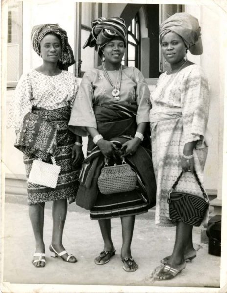 A vintage photograph of three Yoruba women in gele head wraps and traditional dress