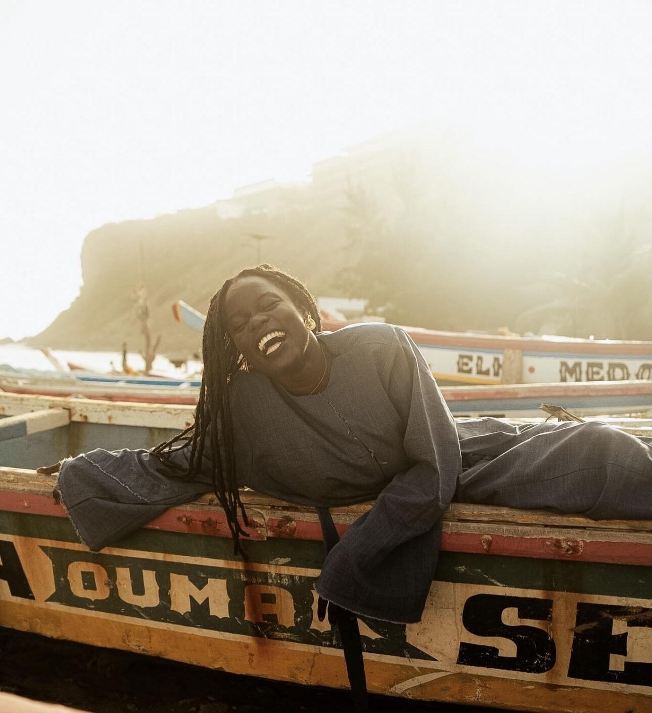 A woman reclining in a painted wooden fishing pirogue on the Dakar coast, sea cliffs behind her