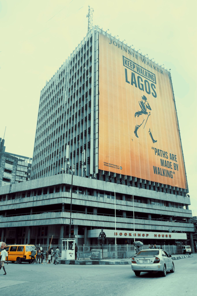 Bookshop House on Lagos Island under a large Keep Walking Lagos banner, a yellow danfo at the junction below
