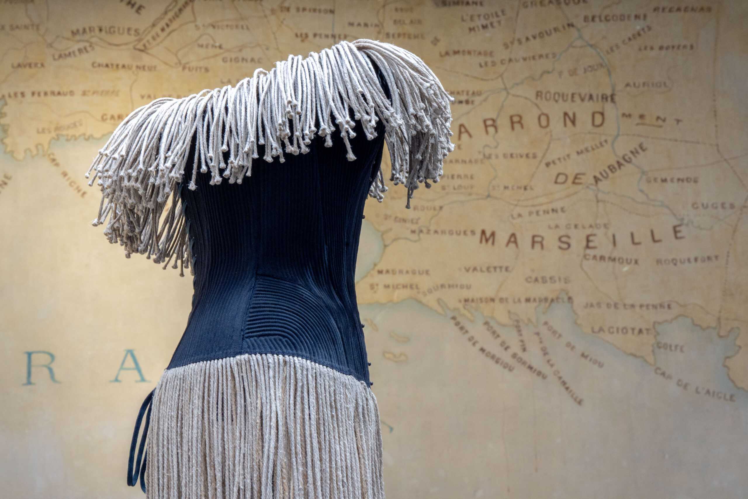 Navy Azzedine Alaïa dress with rope fringe shown against a map of the Marseille coast at the Fondation Azzedine Alaïa