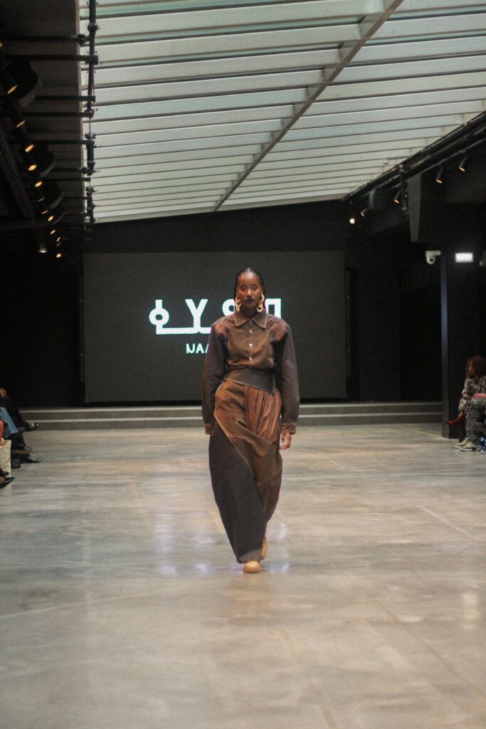 Model walking the runway in a full NAANIYA look beneath the brand logo, SS26 Tombouctou collection at Paris Fashion Week