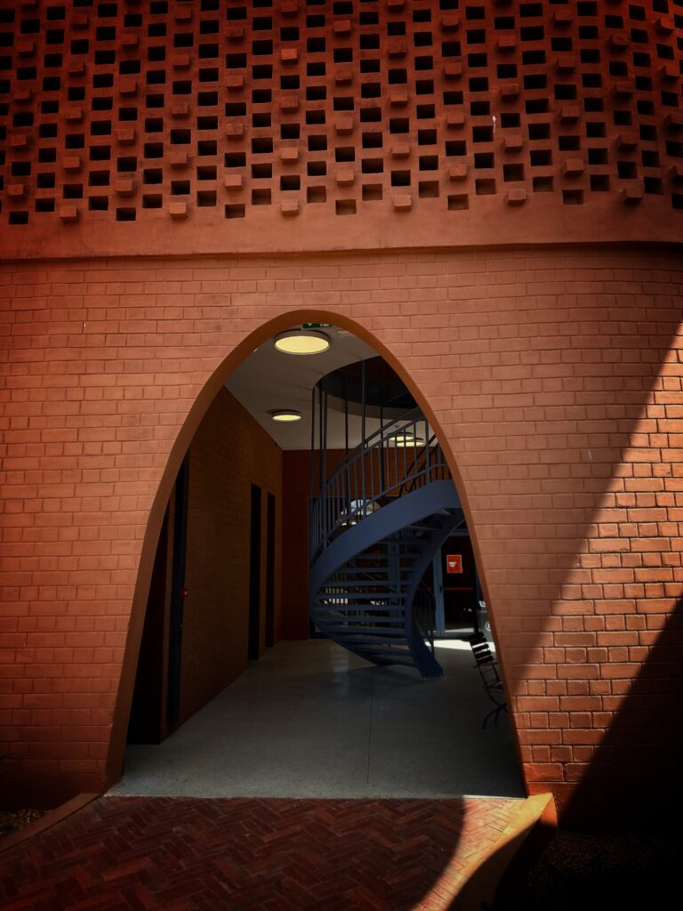 Circular steel staircase meeting the warm laterite walls inside the Goethe-Institut Dakar
