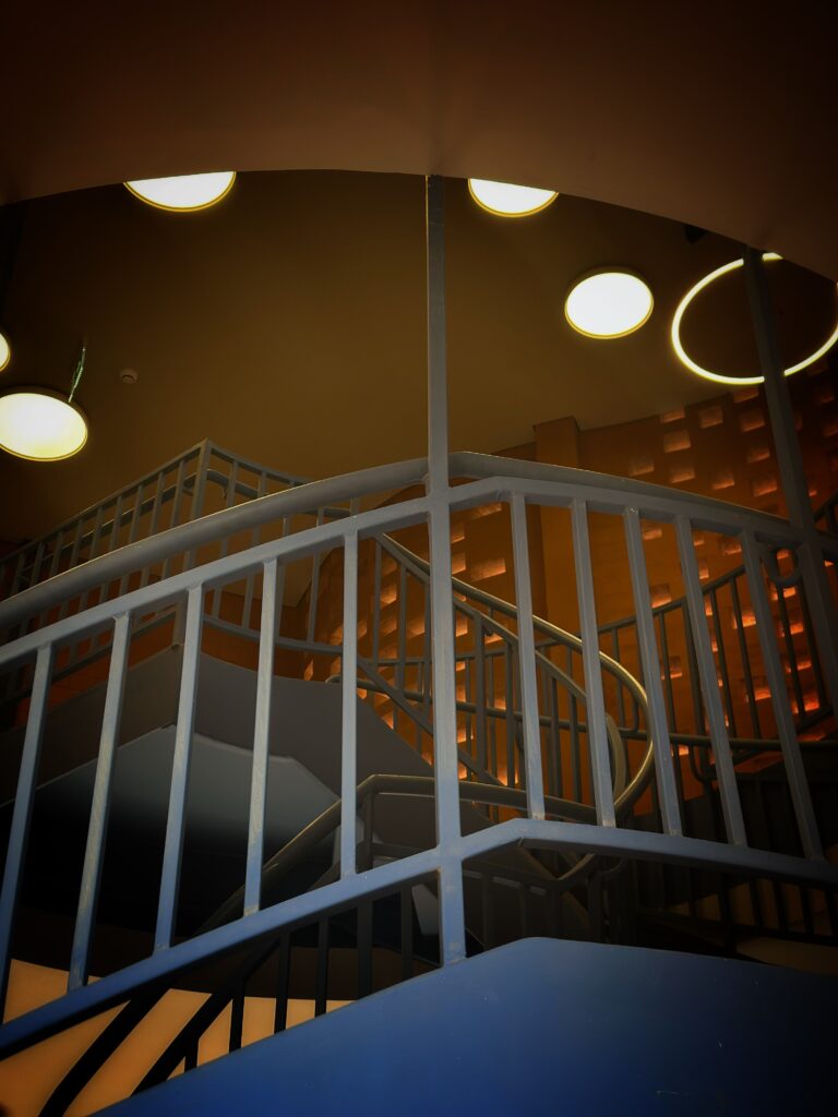 Indoor-outdoor stairwell where a steel staircase meets laterite brick at the Goethe-Institut Dakar