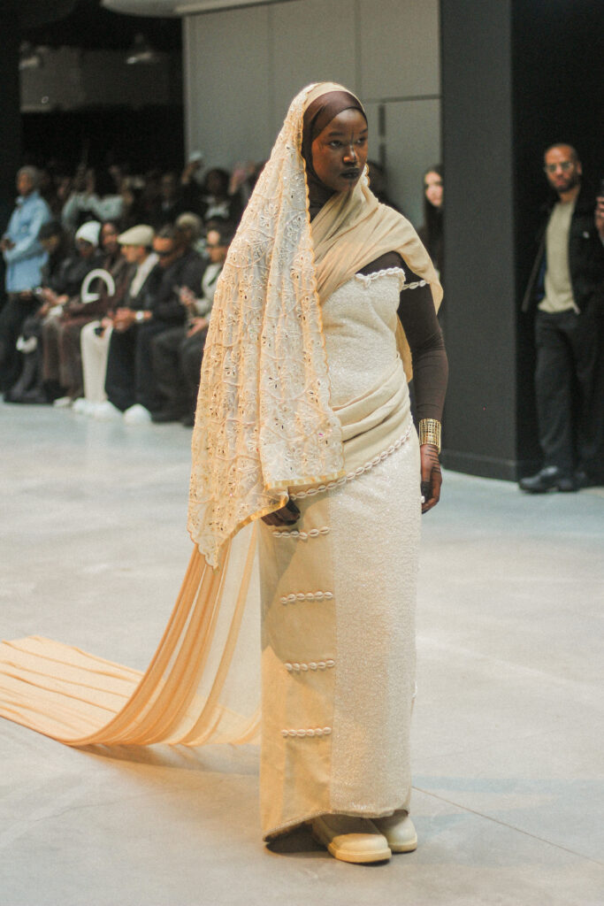 Model in a cream beaded gown with an eyelet-lace shawl and cowrie detailing, NAANIYA SS26 Tombouctou collection
