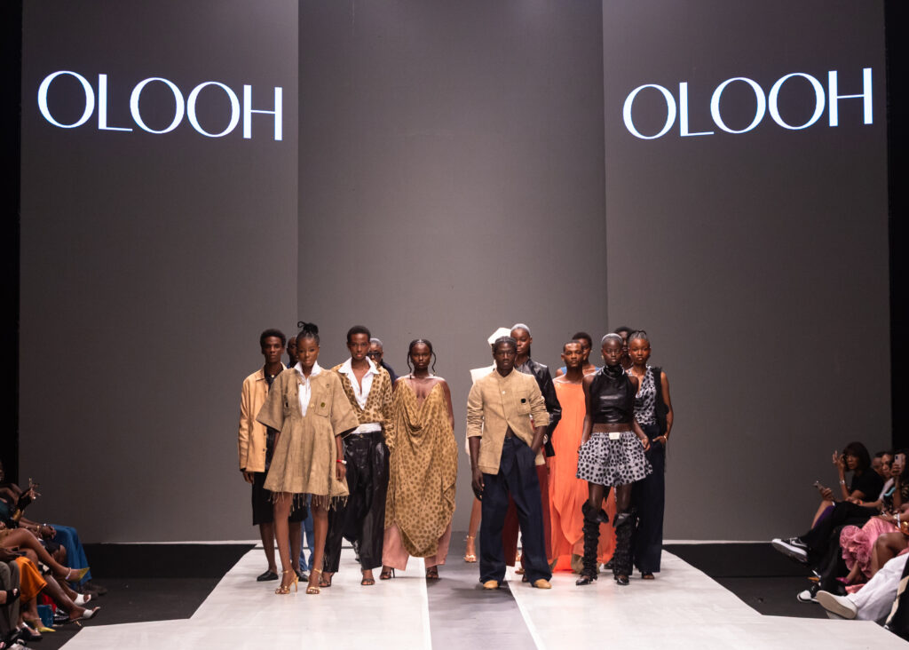 Models at the OLOOH runway finale during Lagos Fashion Week 2025, the label name lit on panels behind them