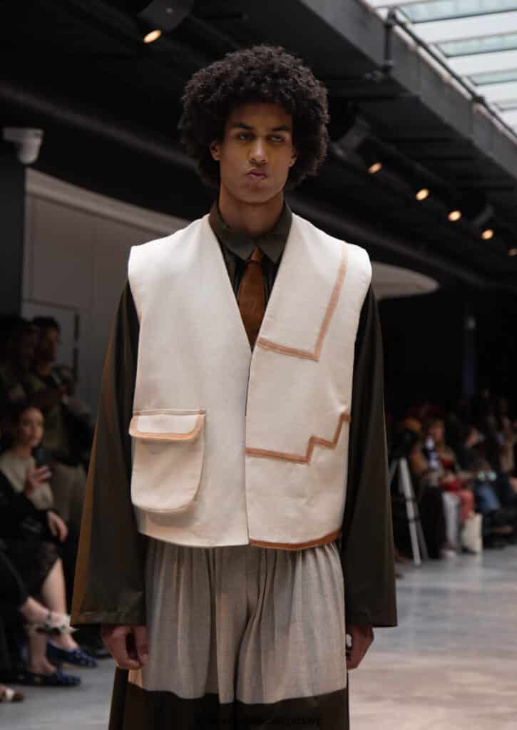 Model in a cream panelled waistcoat over an olive shirt and rust tie, NAANIYA SS26 Tombouctou collection
