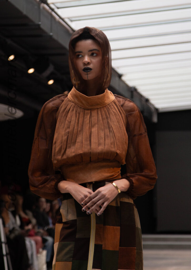Model in a caramel-brown pleated NAANIYA top with gathered high neckline, SS26 Tombouctou collection at Paris Fashion Week