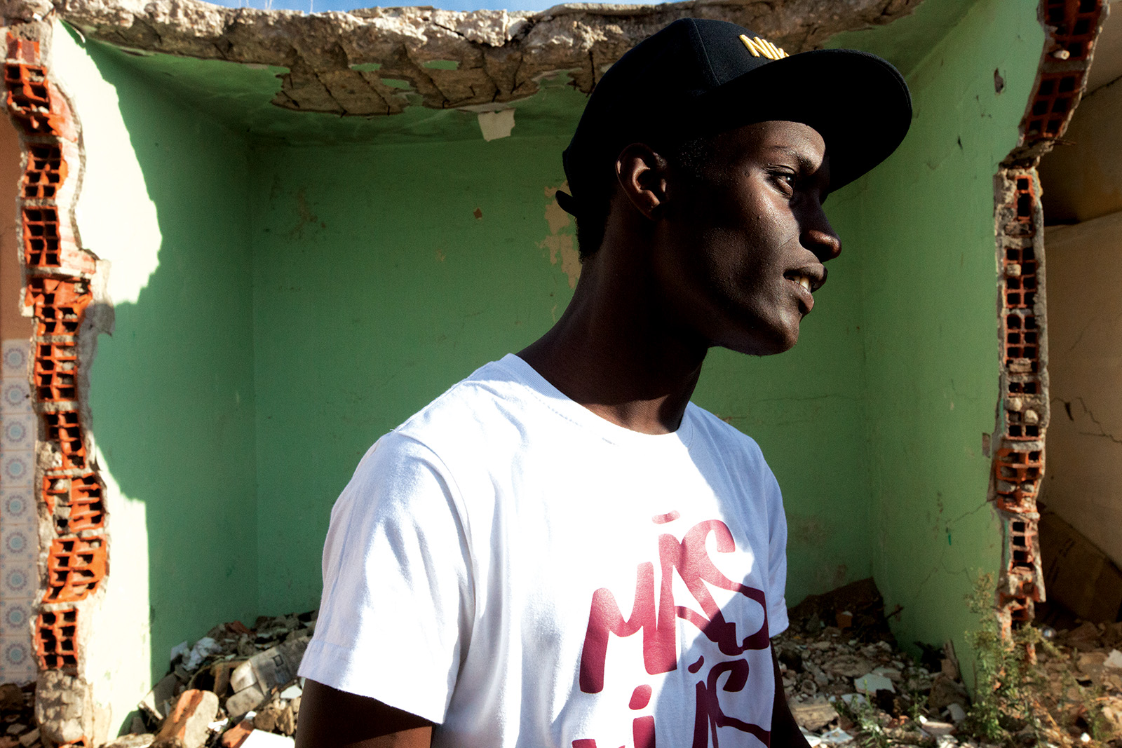 A young man stands inside a partly demolished house with green walls and exposed brick in Bairro 6 de Maio, Amadora.