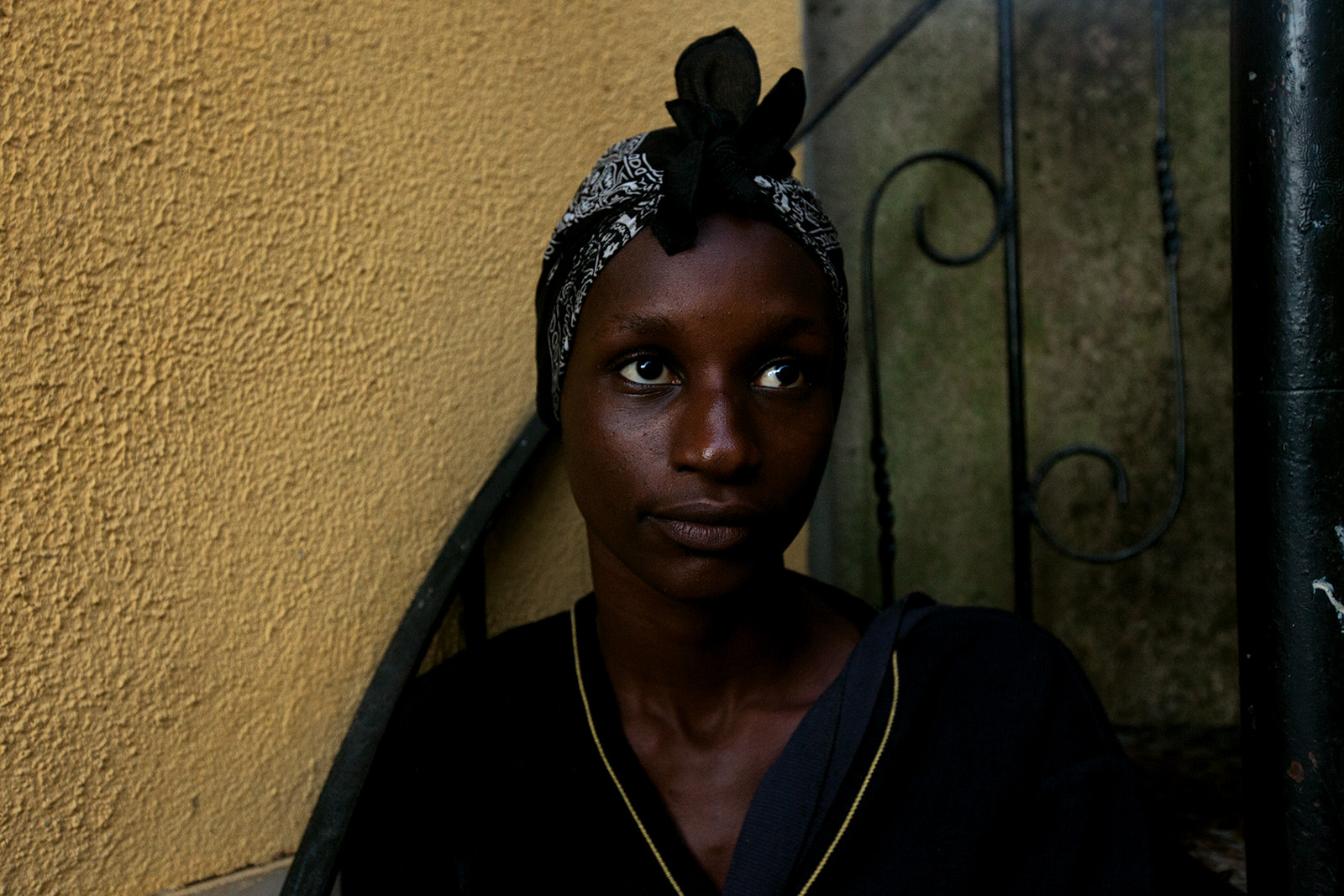 Portrait of a young woman in a patterned headwrap against an ochre wall in Bairro 6 de Maio, Amadora.