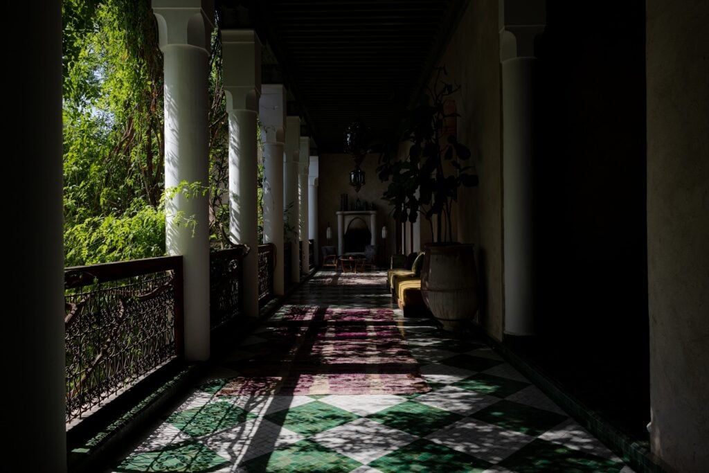 A colonnaded gallery at El Fenn, Marrakech, with dappled light on a green and white tiled floor.