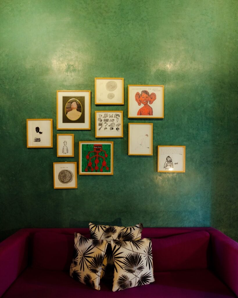 A salon-style gallery wall of framed artworks on a green tadelakt wall at El Fenn, Marrakech.