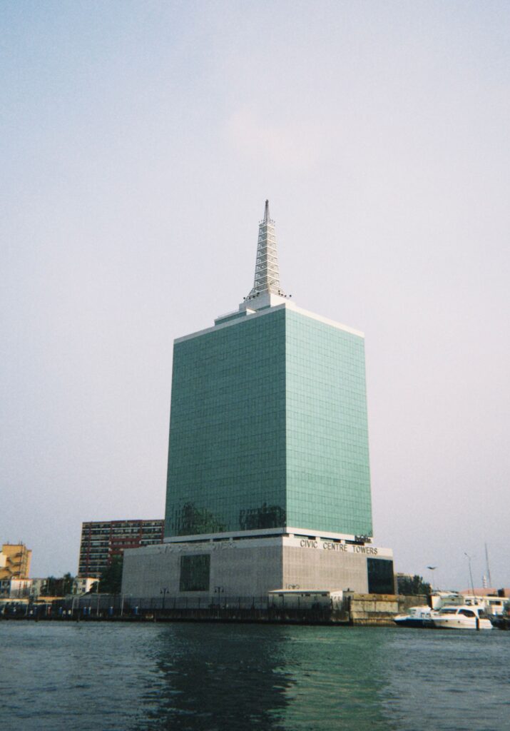 Civic Centre Towers in Lagos, a green glass tower with a stepped spire, seen across the water with boats moored below