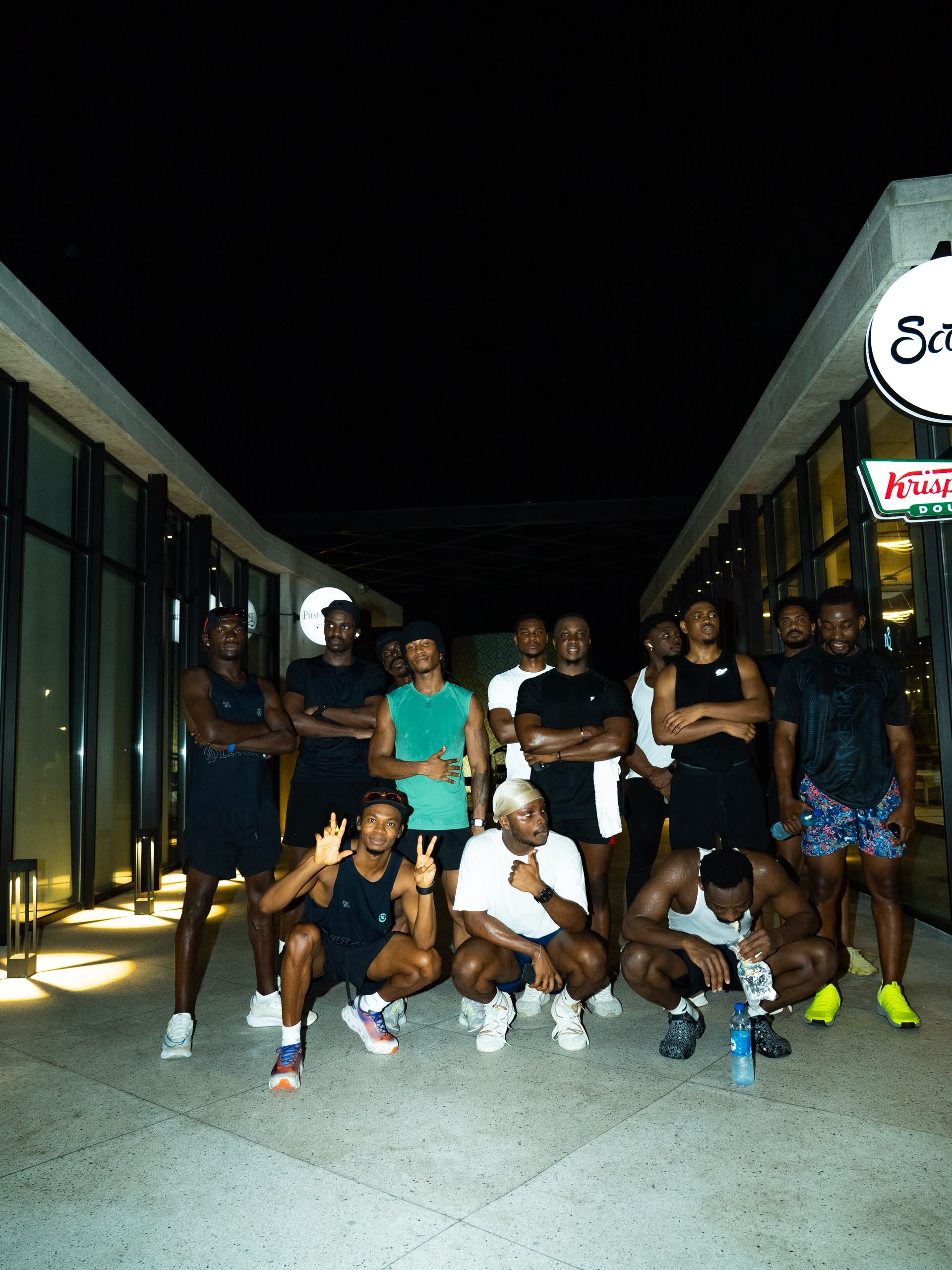 About fifteen runners crouch and stand for a group photograph at night in a lit covered walkway of a shopping arcade.