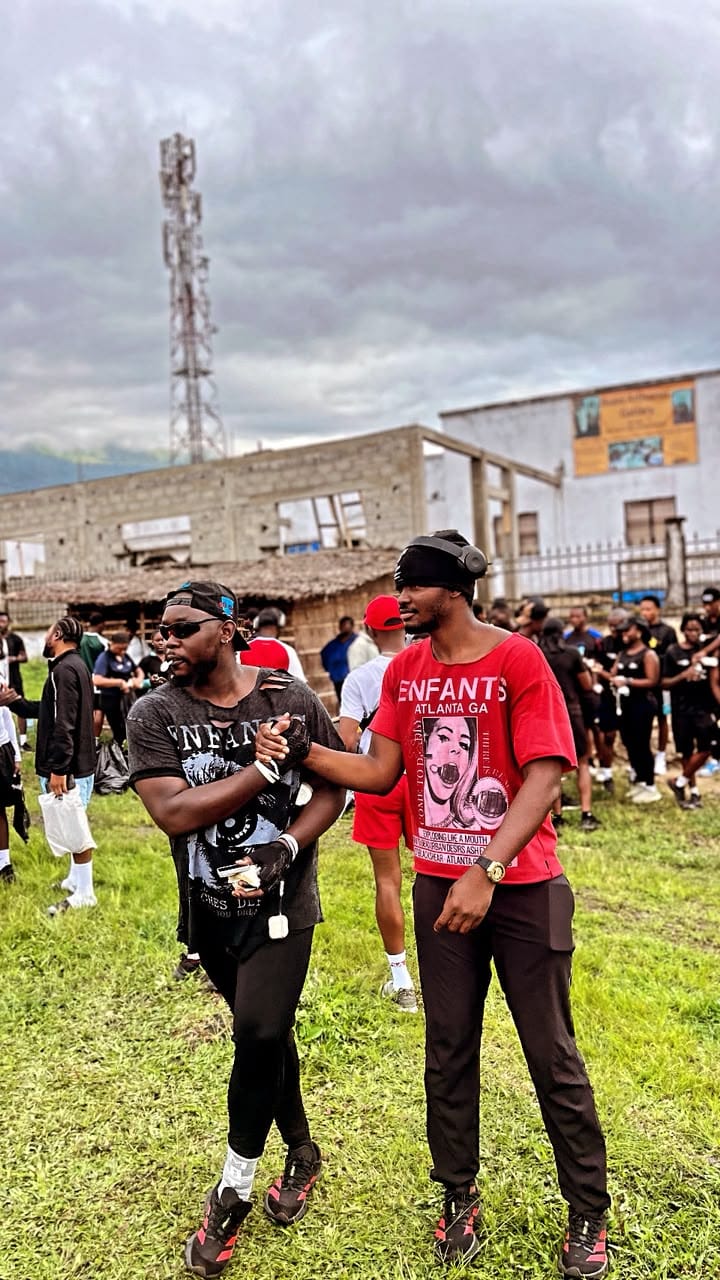 Vintage Run Club co-founders Joseph Junior Gwan and Tati Telvin standing in an open field in Buea, the club in black kit gathered behind them.