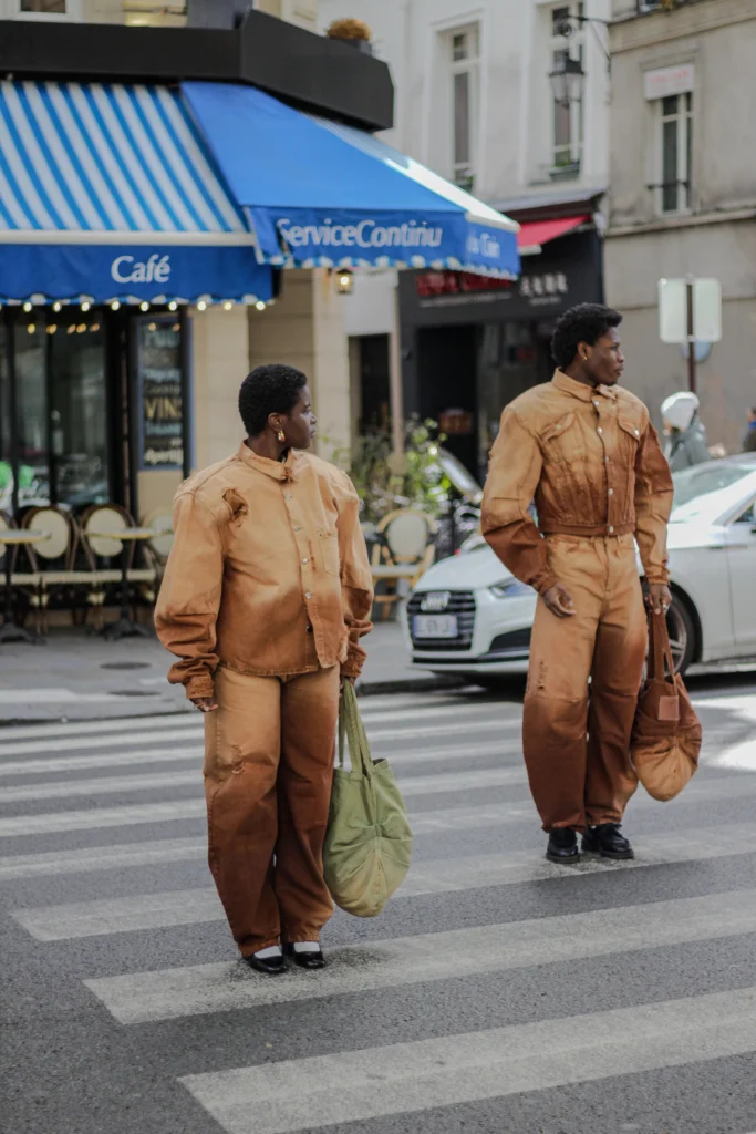 Celebrating Roots and Defying Borders: The Journey of Bledard - African Denim Revolution 2 Two models in rust workwear sets crossing a Paris street with a shopping bag