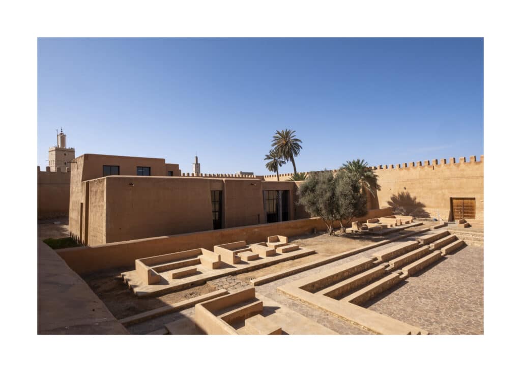 The Tiznit Heritage Interpretation Centre, a low earth-built pavilion set behind the town's crenellated pise ramparts, with a stepped stone courtyard and palms.