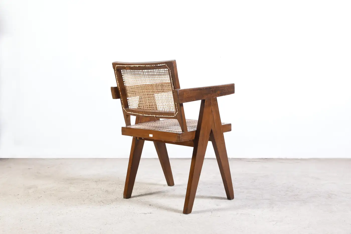 Rear view of a Pierre Jeanneret Chandigarh chair showing V-shaped teak legs and cane back