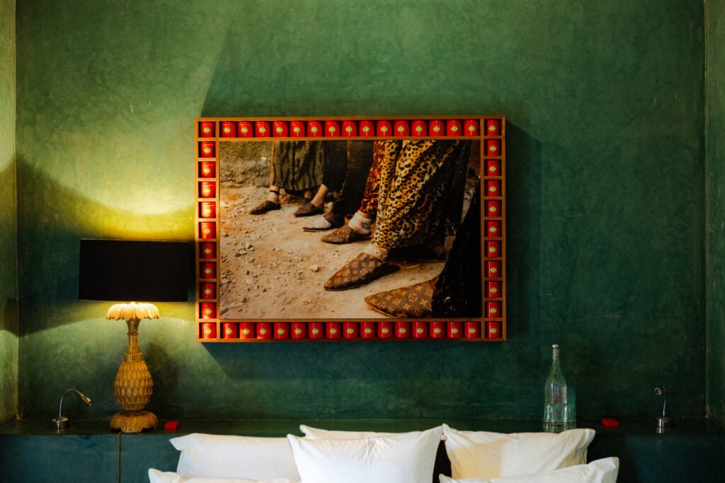 A guest room at El Fenn, Marrakech, with deep green tadelakt walls and a framed artwork in an illuminated red frame above the bed.
