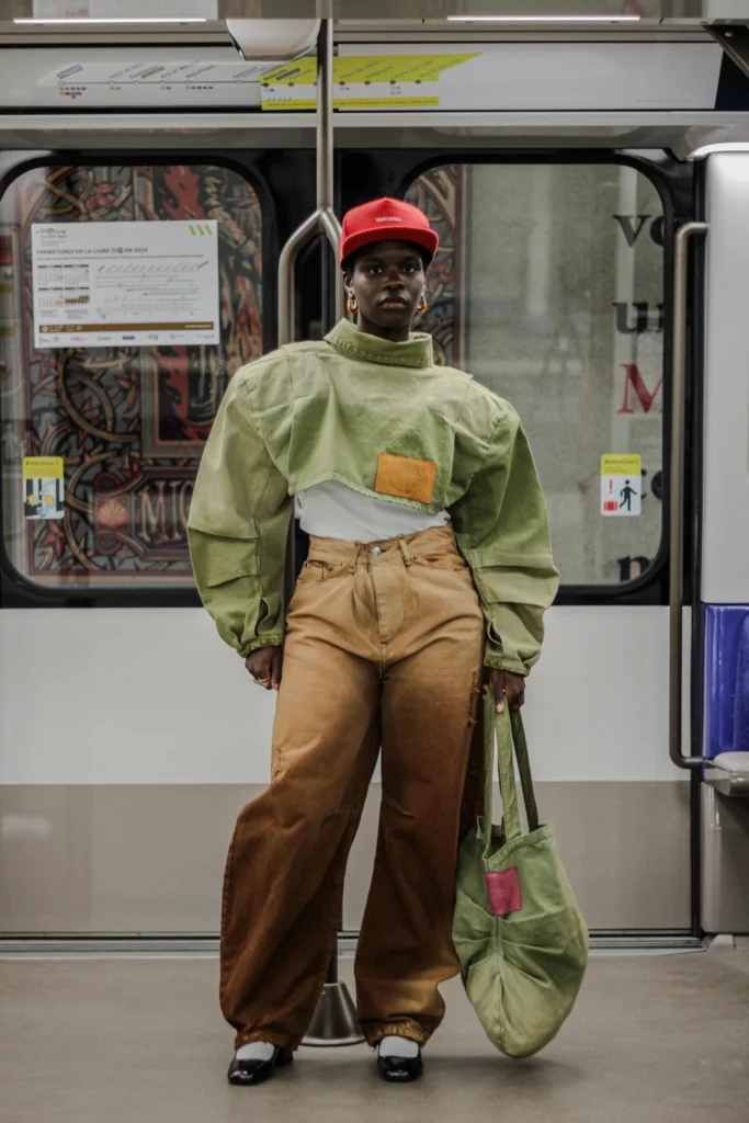 Celebrating Roots and Defying Borders: The Journey of Bledard - African Denim Revolution 4 A model in a printed green top and tan trousers standing in a Metro carriage