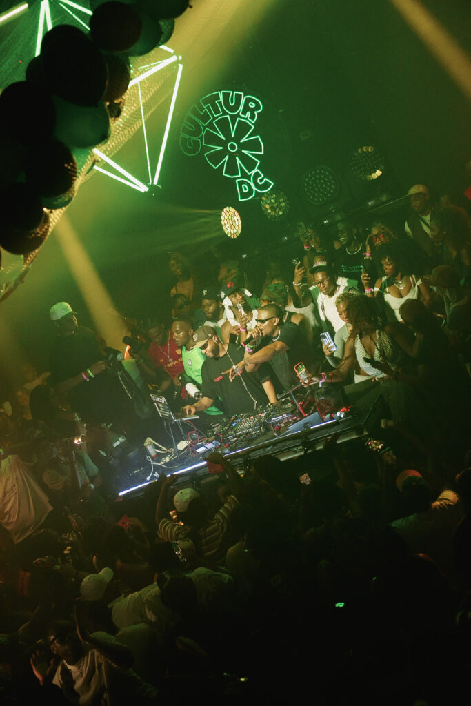 How DJs Helped Take Afrobeats Global 5 Packed dance floor lit green from above, the DJ booth ringed by the crowd beneath the CULTUR neon sign