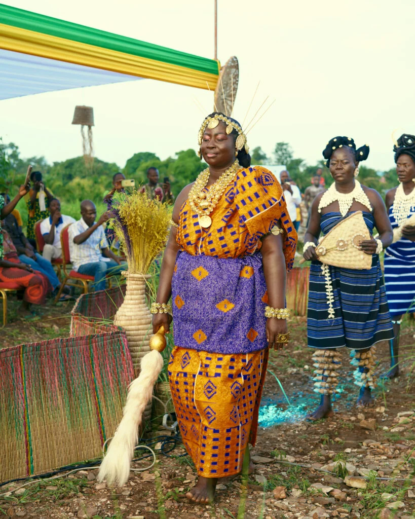 A Heal by Hair ambassador in a gold beaded headdress and orange and blue wax print wrapper parades in traditional attire during the festival in Siou, Togo