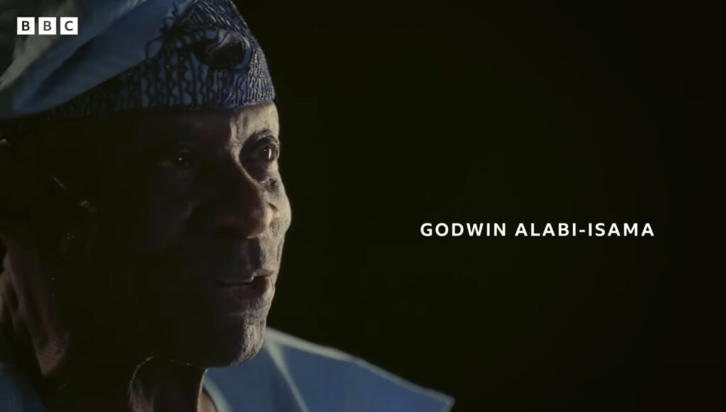 Nigerian civil war veteran Godwin Alabi-Isama, the director's grandfather, filmed in close-up in a patterned blue cap with his name captioned on screen.