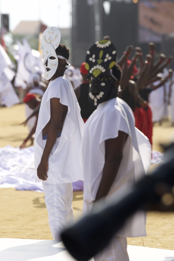 Young performers wearing handmade masks of painted cardboard and cowrie shells at the festival