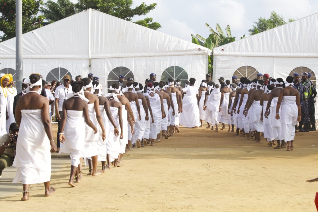 Women dressed in white file between festival tents before the procession at the Festival des Masques in Porto-Novo, Benin