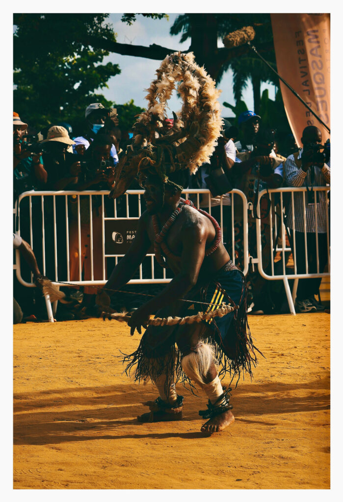 Dancer in a horned headdress performing in front of a line of photographers