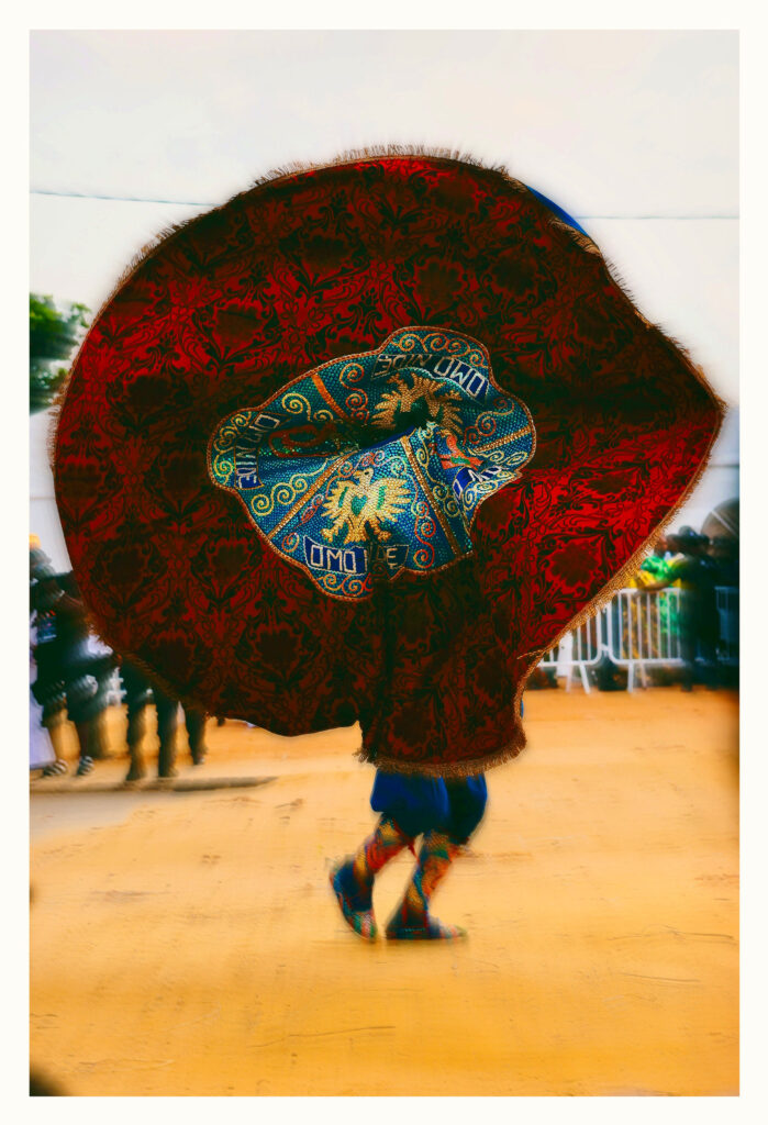 Masquerade opening its beaded cape into a full circle with a central panel reading Omo Nide