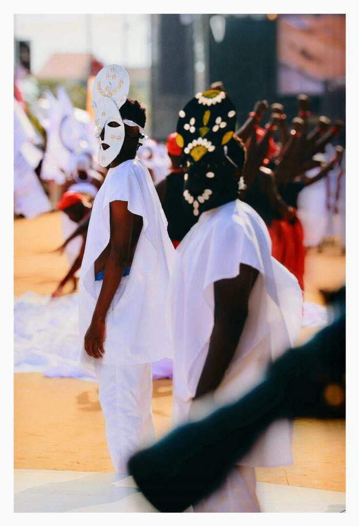 Young performers wearing masks made of painted cardboard and cowrie shells