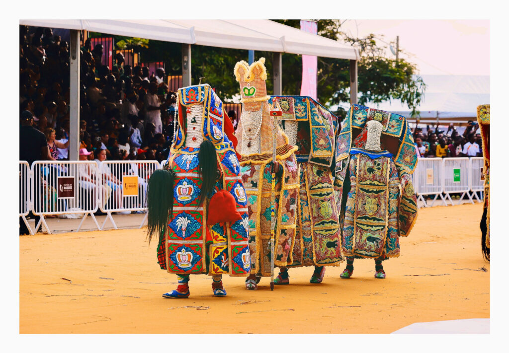 Four masquerade figures crossing the arena in front of the festival grandstand