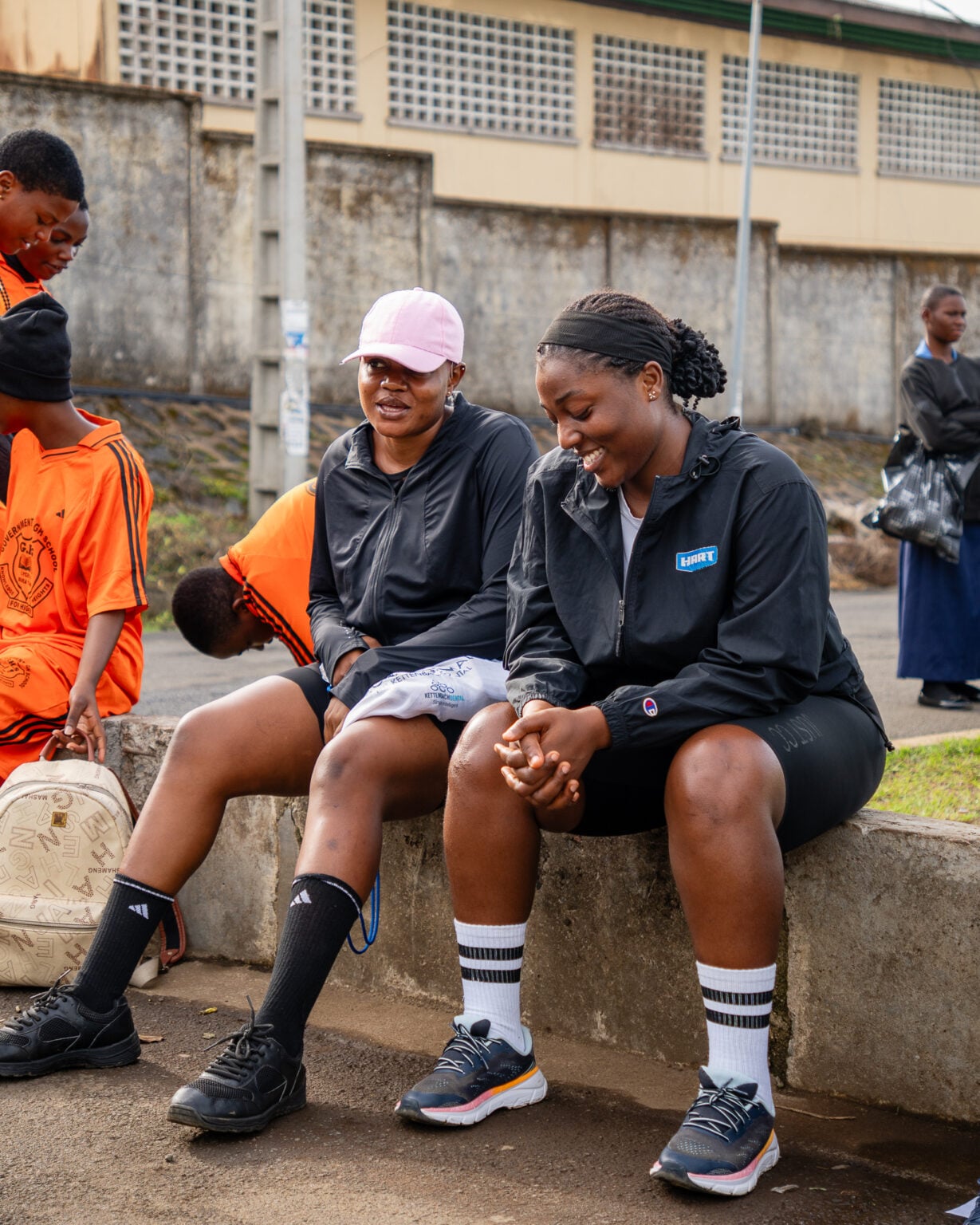 Vintage Run Club members resting on a low wall during a Saturday session in a public space in Buea, other users of the square around them.