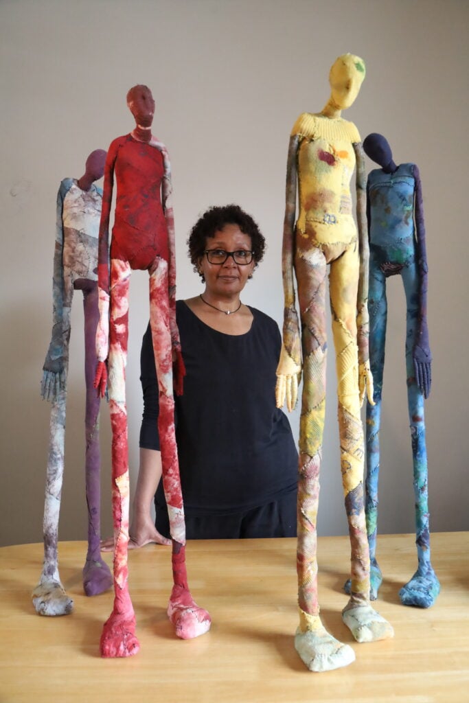 Portrait of Sudanese visual and textile artist Fayrouz Omer beside her artwork