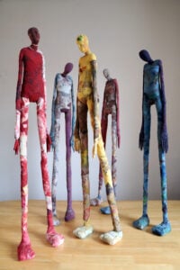 A row of standing textile figures wrapped in stitched cloth in red, grey, yellow and blue, from the Of Roots and Routes exhibition of Sudanese women artists