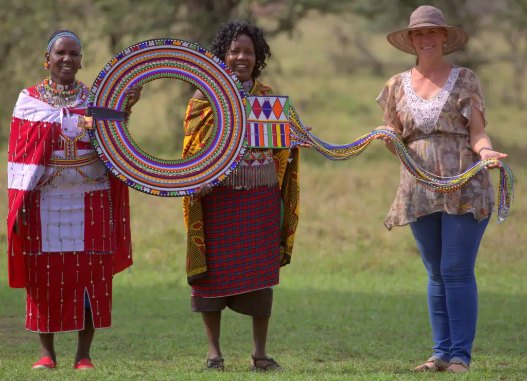Maasai women holding up the Enkarewa, a large beaded collar made by Noormesuku Kereto, at Naboisho Camp in the Maasai Mara, 2019