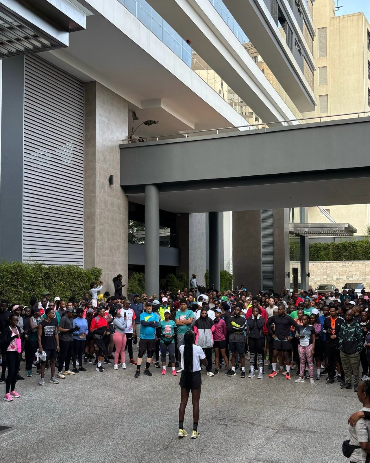 A large crowd of runners fills a road beneath a concrete flyover, one woman in dark kit ahead of the pack.