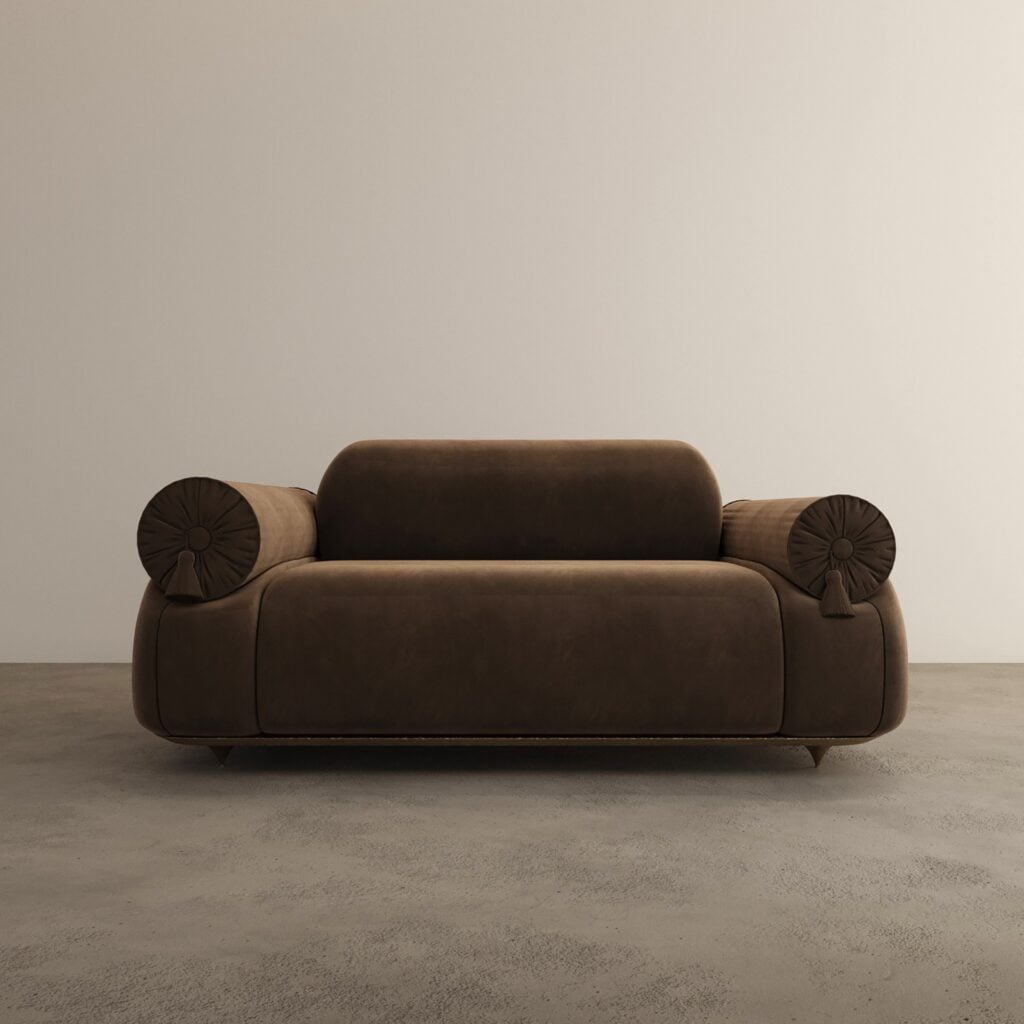 Irtah!, a low two-seat sofa in dark brown upholstery with rounded bolster arms ending in coiled discs, on a pale concrete floor.