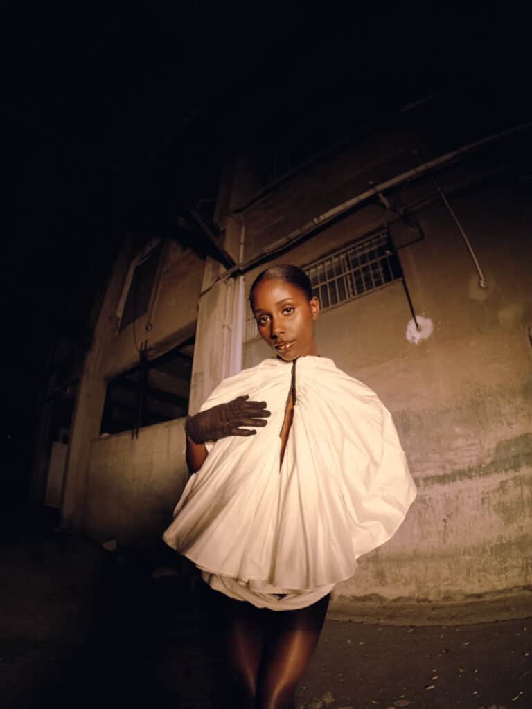 Night portrait of a woman in a voluminous white cape and long black glove outside a weathered building