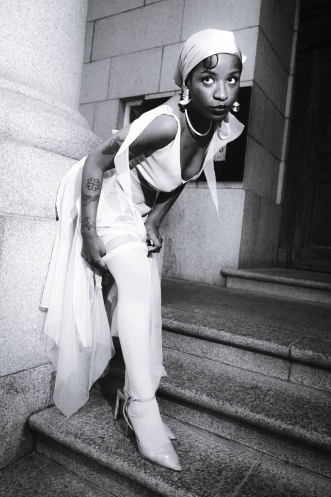 Woman in a white headwrap bending over stone steps, sheer fabric trailing