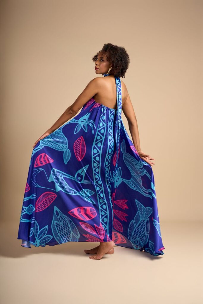 From Korhogo Cloth to Digital Print: Alia Baré and the Language of Senufo Textiles 4 Model seen from behind holding out the skirt of a blue halter-neck dress printed with pink and light-blue Senufo-inspired figures.
