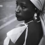 Black-and-white close-up portrait of a woman in a white headwrap on a city street