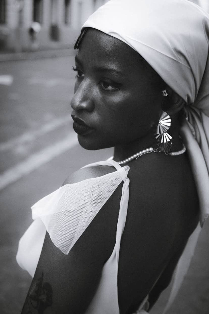 Black-and-white close-up portrait of a woman in a white headwrap on a city street
